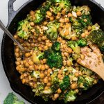a black cast iron skillet of vegan broccoli cashews and chickpeas with garlic sauce.