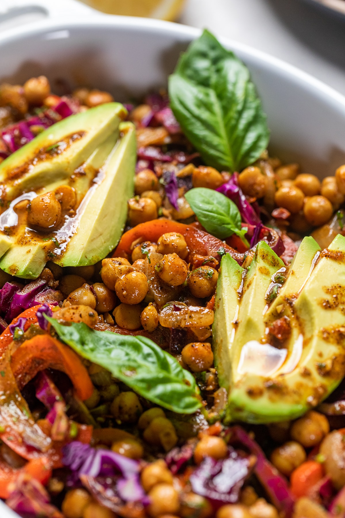 vegan turkish chickpea salad in a white casserole dish topped with avocado and basil.