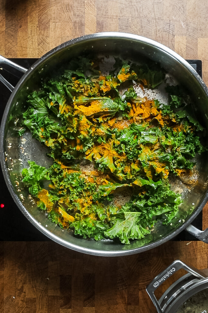 A skillet of uncooked kale, turmeric, garlic powder, salt, and black pepper.