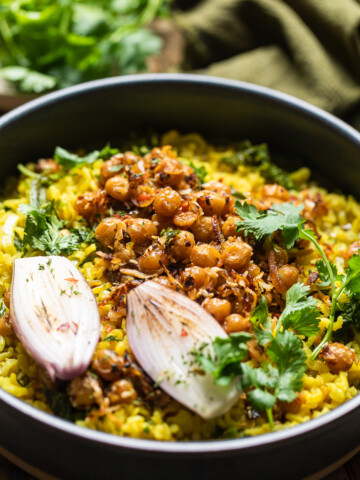 A blue bowl of creamy coconut rice with spiced chickpeas and fresh herbs and shallots.