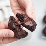 a hand breaking apart a dairy free triple chocolate cookie.