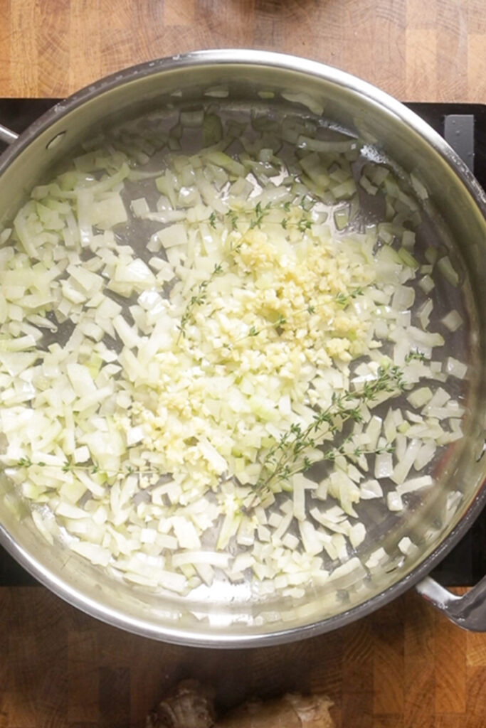 A pot of onions, thyme, garlic, and ginger cooking.