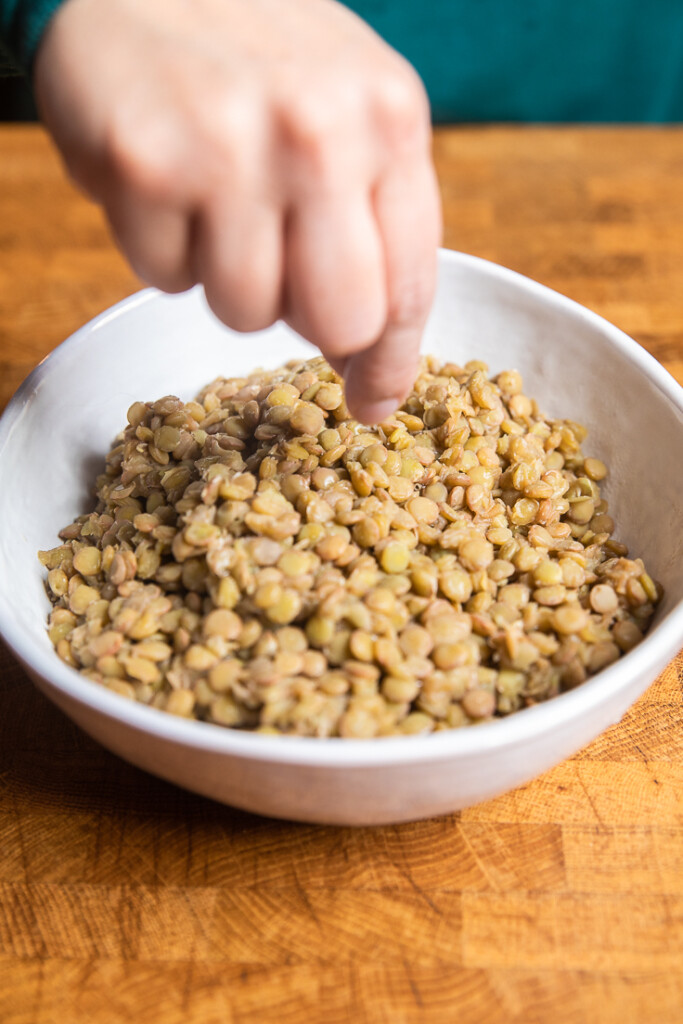 A white bowl of cooked brown lentils.