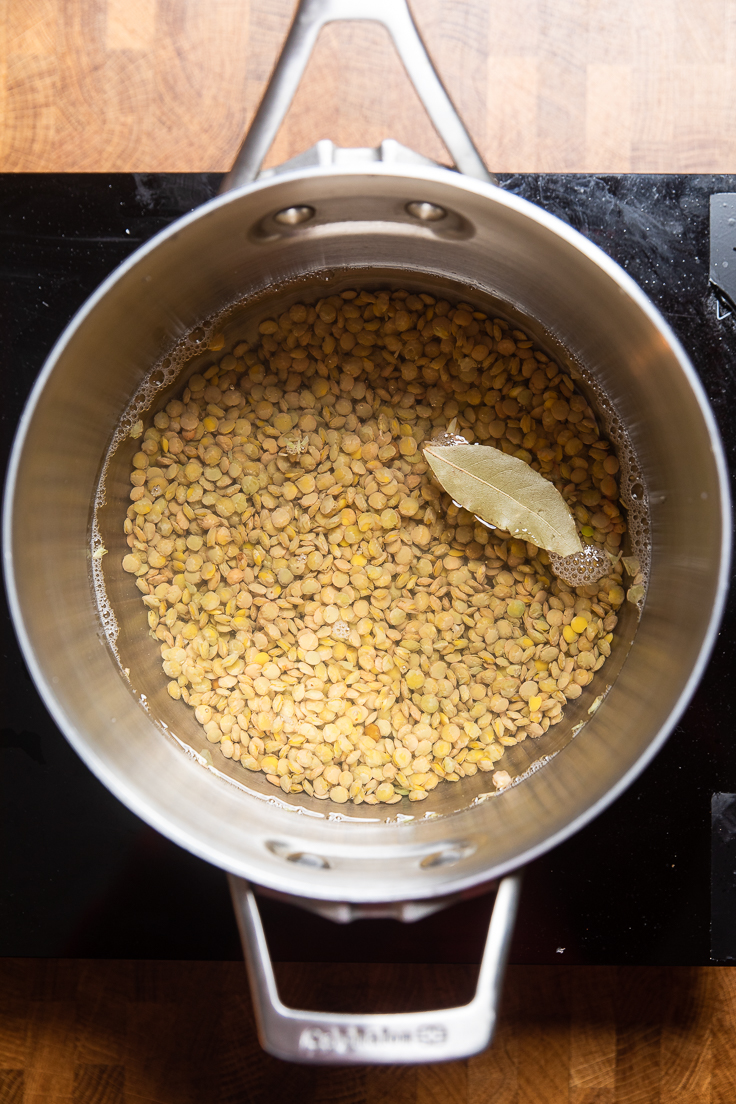 Lentils in a simmering pot of water with a bay leaf on top.