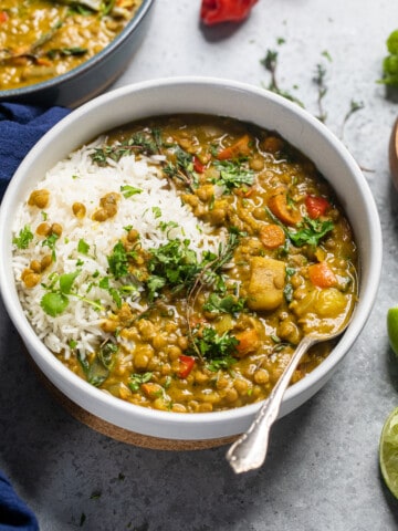 white bowl of jamaican lentil curry with side of rice.