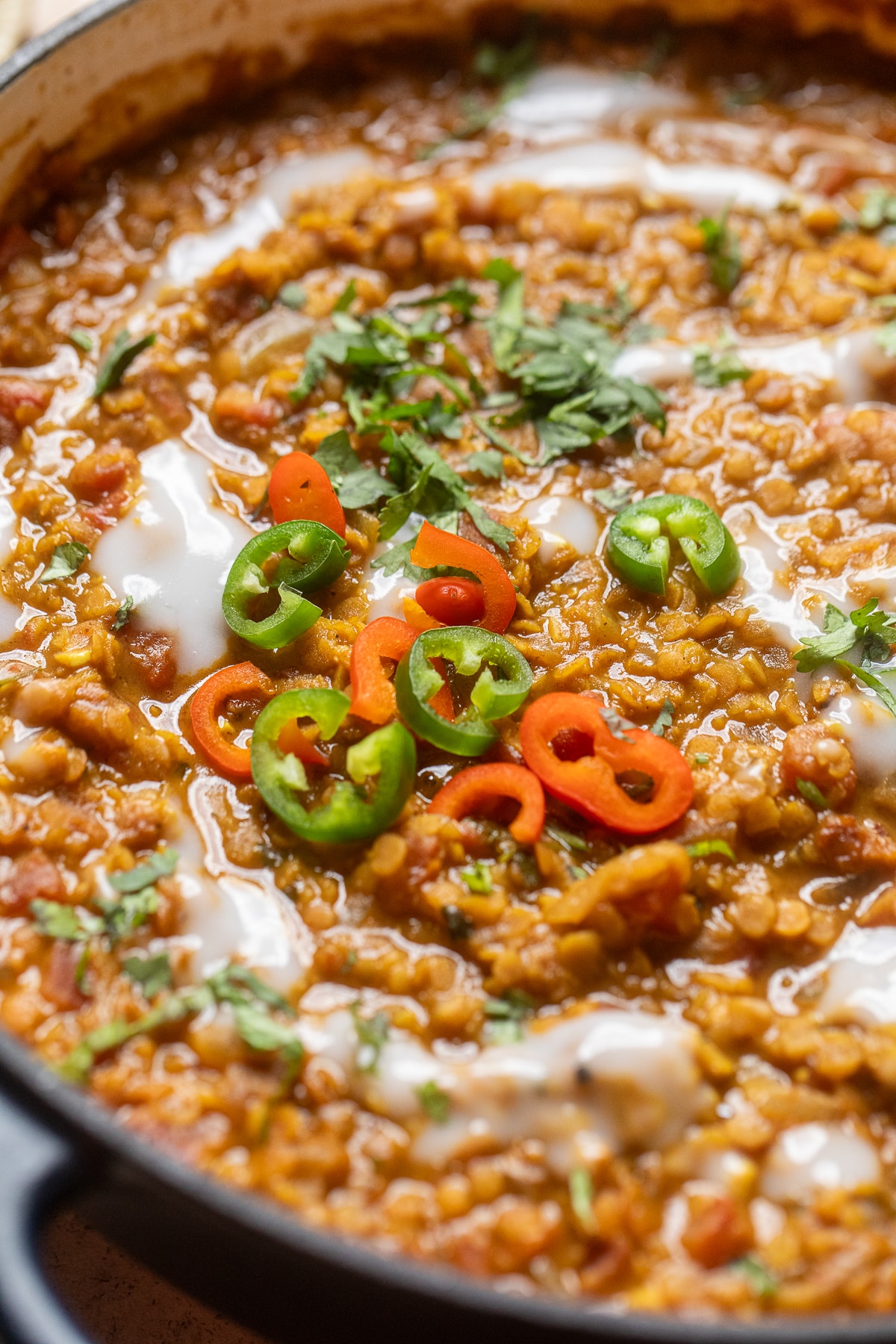 close up of masoor dal in a skillet with fresh chilis and herbs.