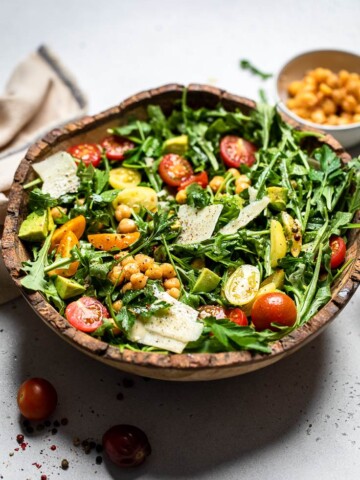 Vegan arugula salad with chickpeas, avocado and cherry tomatoes inside a wooden bowl.