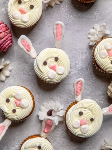 An assortment of Vegan bunny cupcakes on a gray board with white flowers.