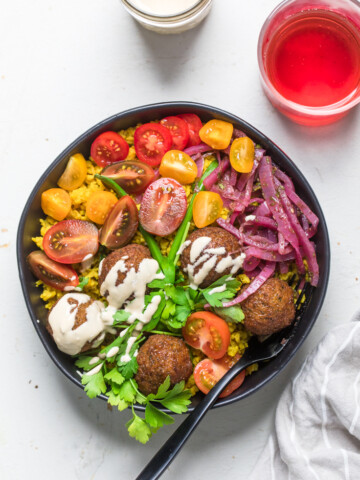 A Vegan Falafel Bowl with fresh tomatoes, red onions, and tahini dressing.