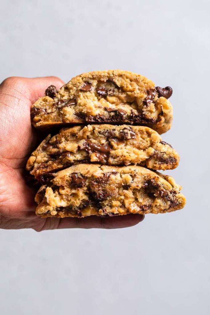Three halves of Vegan Levain chocolate chip cookies stacked in a hand. 