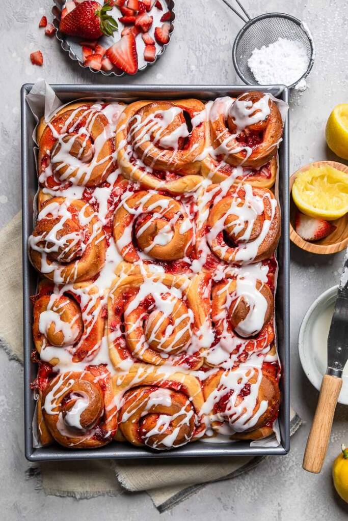 A tray of vegan strawberry cinnamon rolls with a lemon glaze drizzled over the top. 