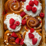 Vegan white chocolate raspberry sweet rolls topped with fresh raspberries and frosting.